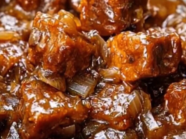 Slow-cooker honey garlic beef tips with a glossy, dark sauce and onions in a ceramic serving dish.