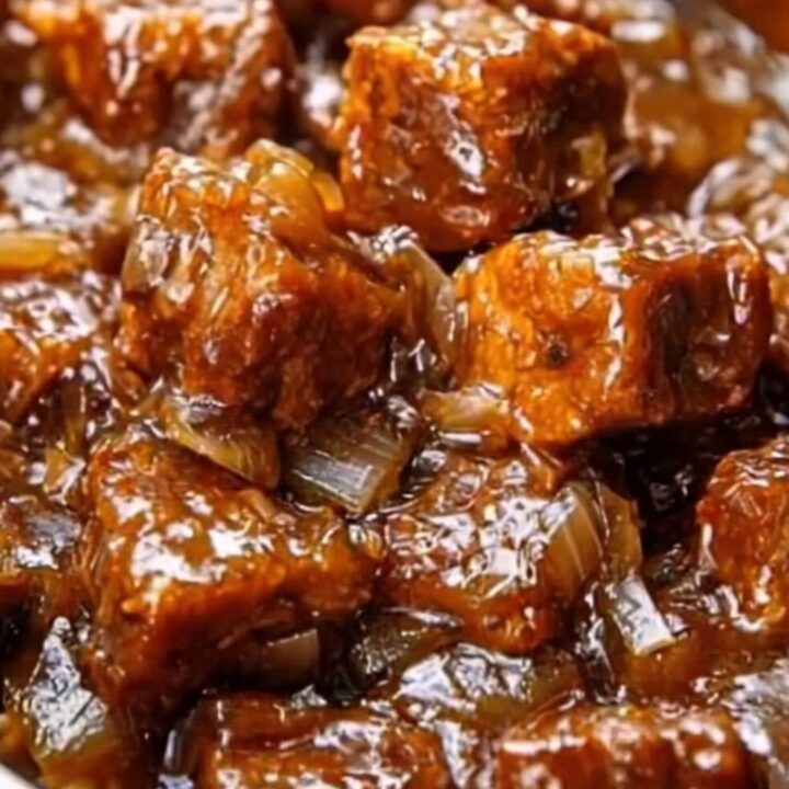 Slow-cooker honey garlic beef tips with a glossy, dark sauce and onions in a ceramic serving dish.