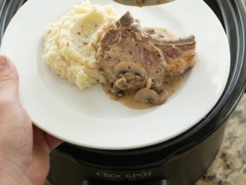 Slow-cooker pork chops in creamy mushroom-ranch sauce with melted Gruyère, in a black crockpot