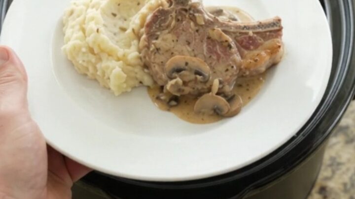 Slow-cooker pork chops in creamy mushroom-ranch sauce with melted Gruyère, in a black crockpot