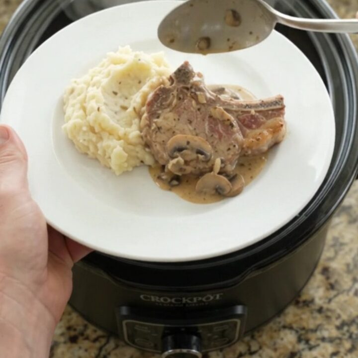 Slow-cooker pork chops in creamy mushroom-ranch sauce with melted Gruyère, in a black crockpot