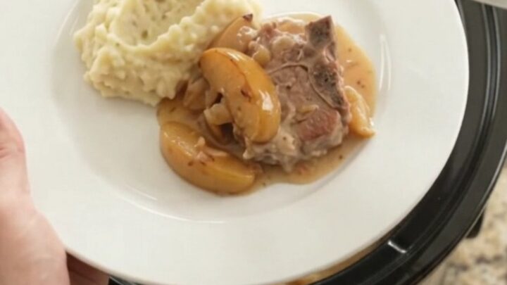 Slow cooker full of bubbling Gruyère apple cider pork chops with apples and cream sauce