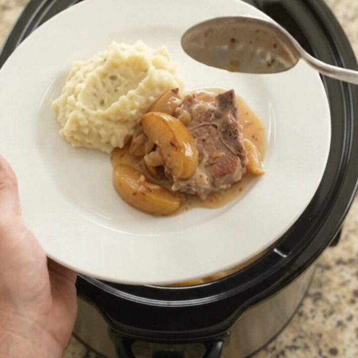 Slow cooker full of bubbling Gruyère apple cider pork chops with apples and cream sauce
