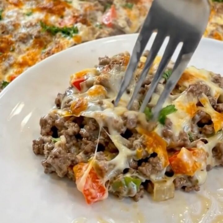 A portion of Philly cheesesteak casserole being lifted with a fork, showing long strings of melted provolone cheese.