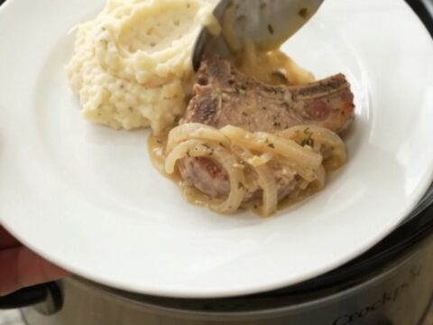 Slow cooker filled with creamy Gruyère onion sauce and tender pork chops, garnished with thyme.