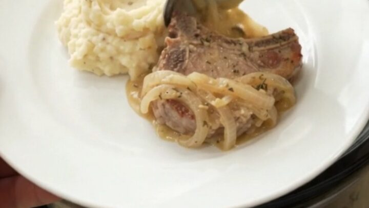 Slow cooker filled with creamy Gruyère onion sauce and tender pork chops, garnished with thyme.