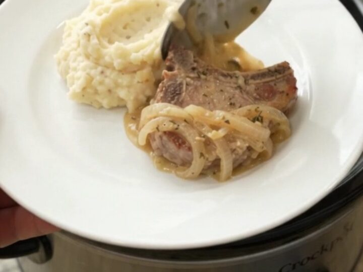 Slow cooker filled with creamy Gruyère onion sauce and tender pork chops, garnished with thyme.