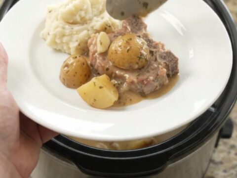 Slow cooker butter cream pork chops and baby potatoes in a glossy black crockpot