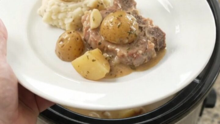 Slow cooker butter cream pork chops and baby potatoes in a glossy black crockpot