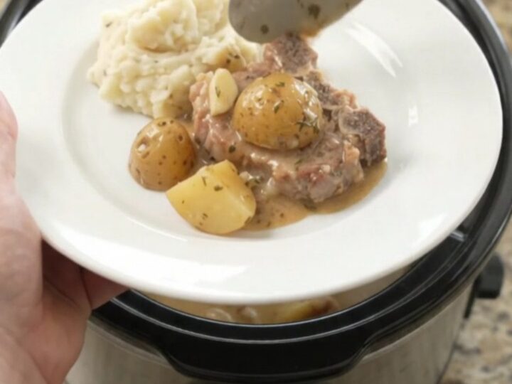 Slow cooker butter cream pork chops and baby potatoes in a glossy black crockpot