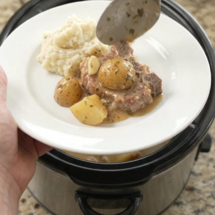 Slow cooker butter cream pork chops and baby potatoes in a glossy black crockpot