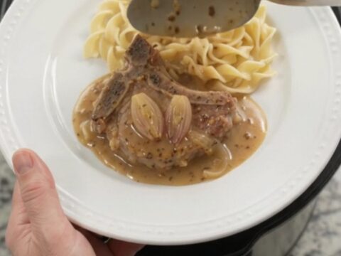 Slow cooker honey Dijon pork chops in a bubbling sauce with shallots, topped with a spoonful of gravy.
