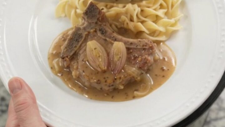 Slow cooker honey Dijon pork chops in a bubbling sauce with shallots, topped with a spoonful of gravy.