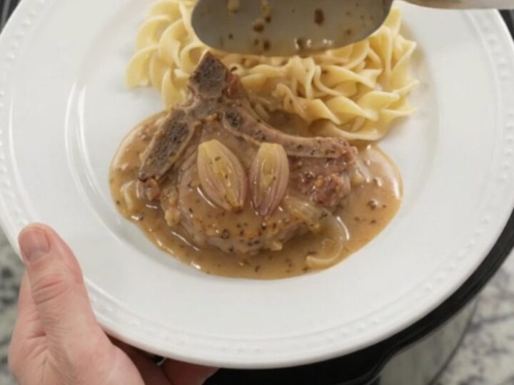 Slow cooker honey Dijon pork chops in a bubbling sauce with shallots, topped with a spoonful of gravy.