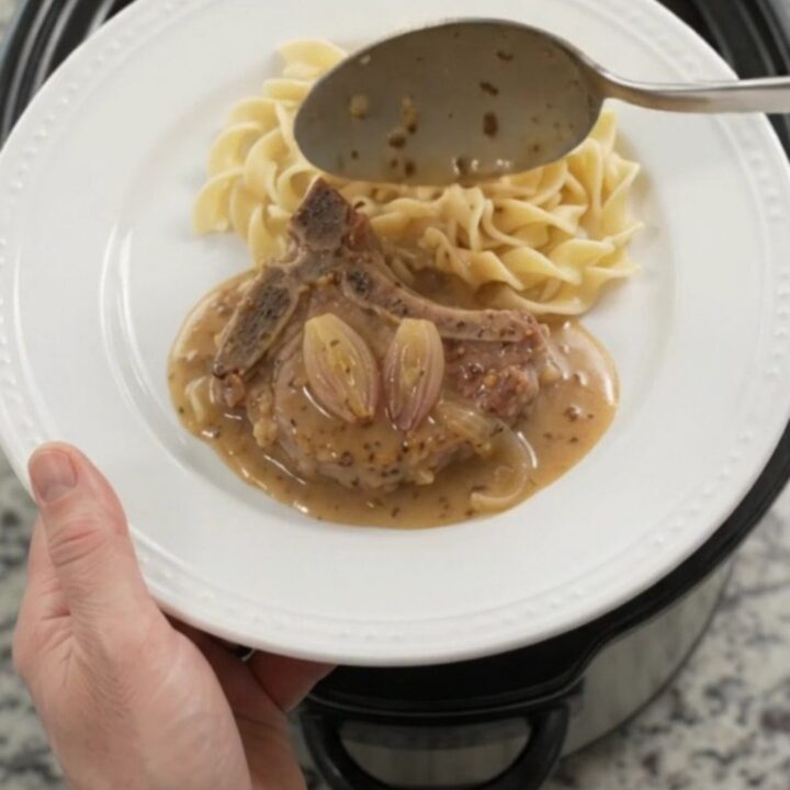 Slow cooker honey Dijon pork chops in a bubbling sauce with shallots, topped with a spoonful of gravy.