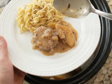 Slow cooker filled with pork medallions, apples, and creamy sauce, steam rising