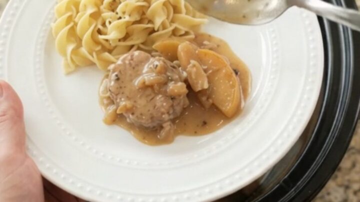 Slow cooker filled with pork medallions, apples, and creamy sauce, steam rising