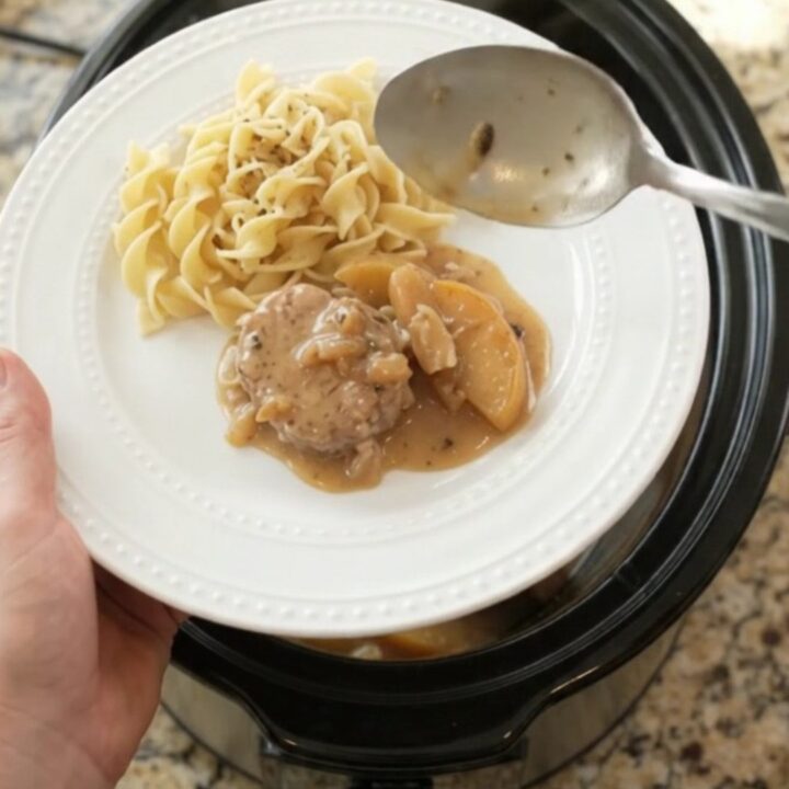 Slow cooker filled with pork medallions, apples, and creamy sauce, steam rising