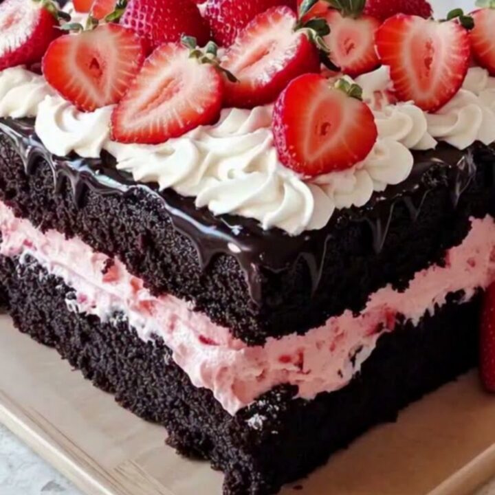 A decadent square chocolate cake topped with whipped cream rosettes and fresh strawberries.