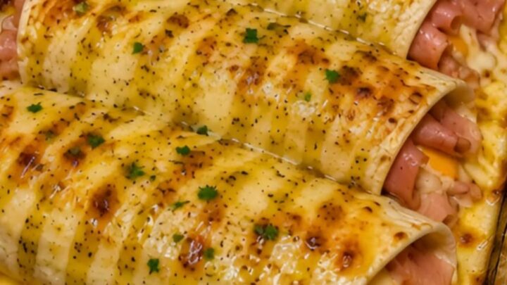 Four golden-brown honey mustard ham and cheese wraps in a glass baking dish with fresh parsley garnish.