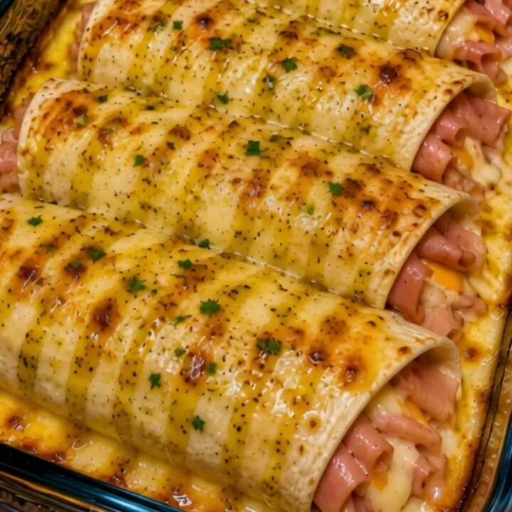 Four golden-brown honey mustard ham and cheese wraps in a glass baking dish with fresh parsley garnish.