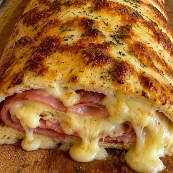 A golden-brown braided ham and cheese stromboli resting on a wooden board with melted cheese oozing out.