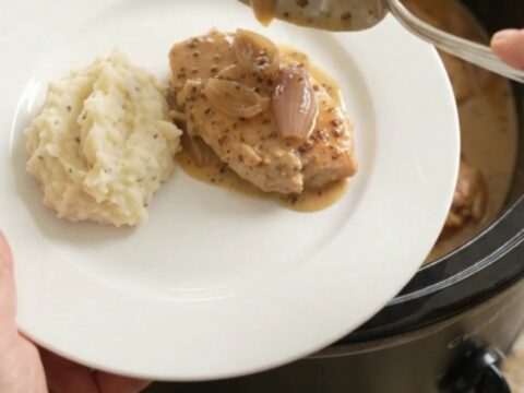 Slow cooker honey Dijon turkey cutlets in a creamy sauce, garnished with fresh thyme, in a black crockpot.