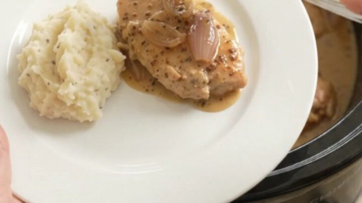 Slow cooker honey Dijon turkey cutlets in a creamy sauce, garnished with fresh thyme, in a black crockpot.
