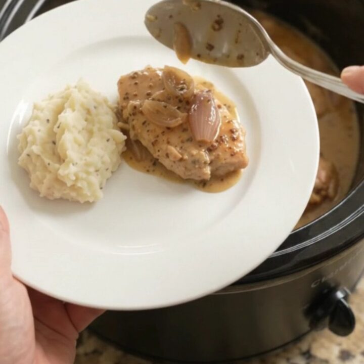 Slow cooker honey Dijon turkey cutlets in a creamy sauce, garnished with fresh thyme, in a black crockpot.