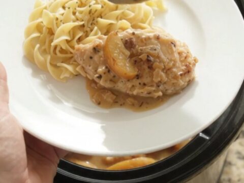 Slow cooker with chicken, apples, and creamy gravy, spoon lifting a portion