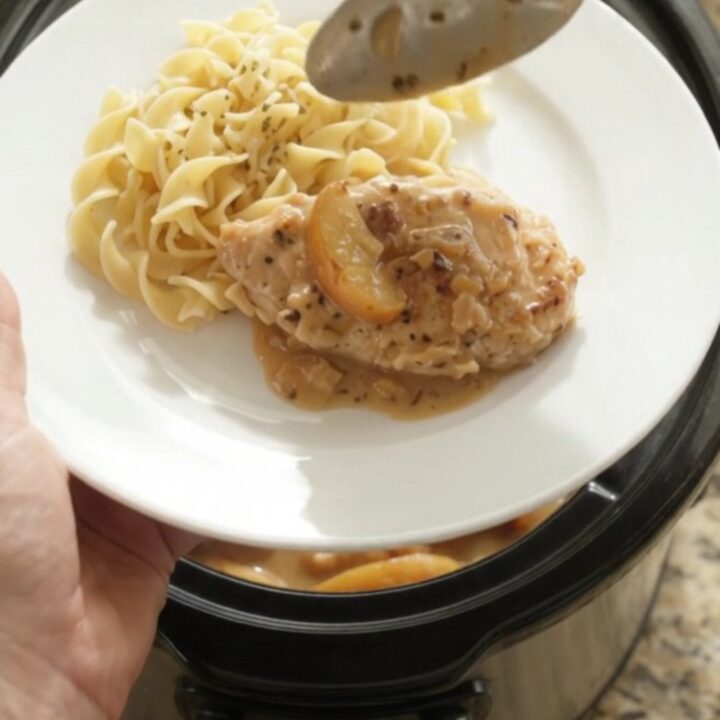 Slow cooker with chicken, apples, and creamy gravy, spoon lifting a portion