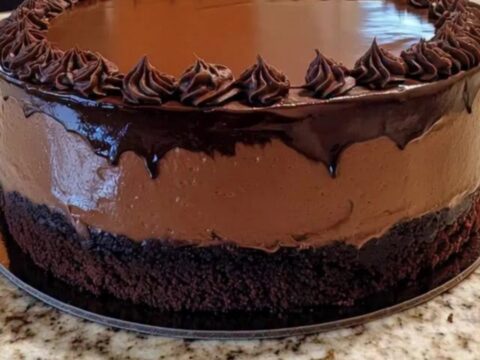 A close-up shot of a chocolate mousse cake with glossy ganache drips and decorative rosettes.