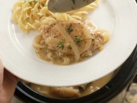 Slow cooker full of sour cream French onion chicken cutlets with onions and thyme