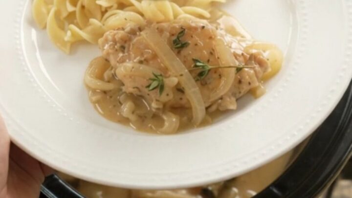 Slow cooker full of sour cream French onion chicken cutlets with onions and thyme