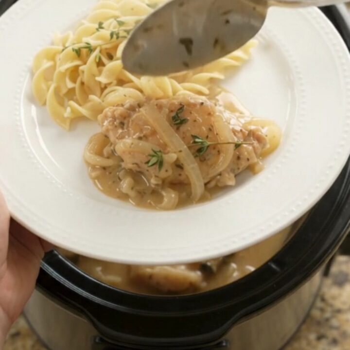 Slow cooker full of sour cream French onion chicken cutlets with onions and thyme