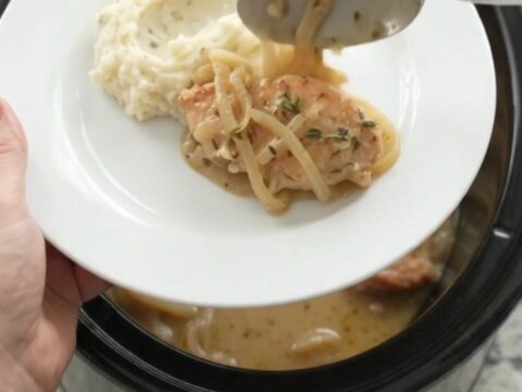 Butter cream French onion chicken cutlets in a slow cooker, topped with melted onions and thyme.