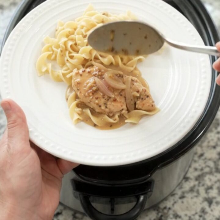Crockpot sour cream honey Dijon chicken cutlets in a black slow cooker, creamy sauce with shallots