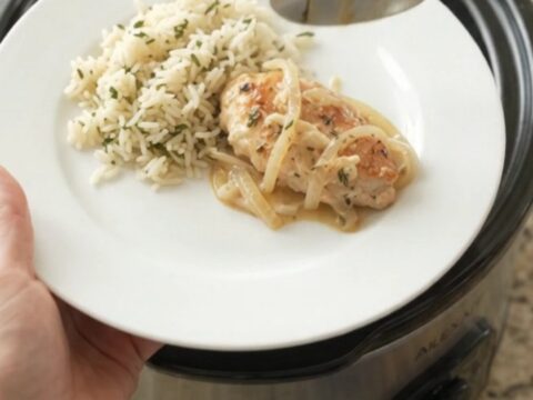 Slow cooker chicken cutlets in a creamy Parmesan onion sauce, with melted onions and thyme in a black Crockpot