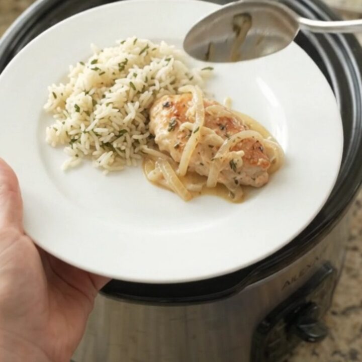 Slow cooker chicken cutlets in a creamy Parmesan onion sauce, with melted onions and thyme in a black Crockpot