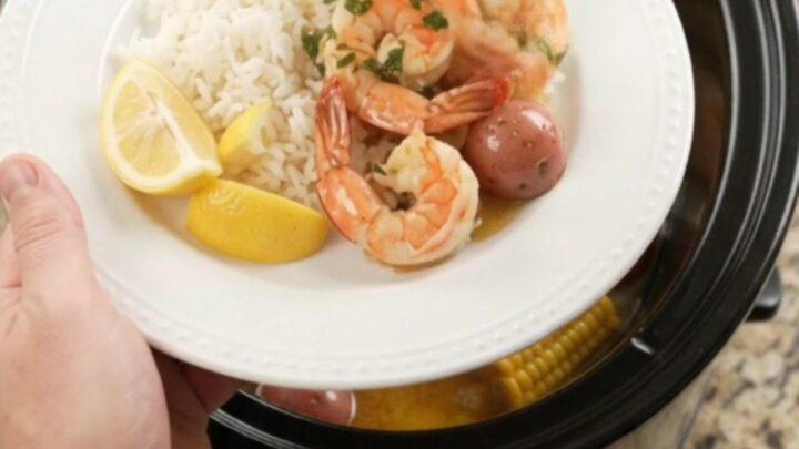 Slow cooker filled with shrimp, corn, and potatoes in a golden butter sauce