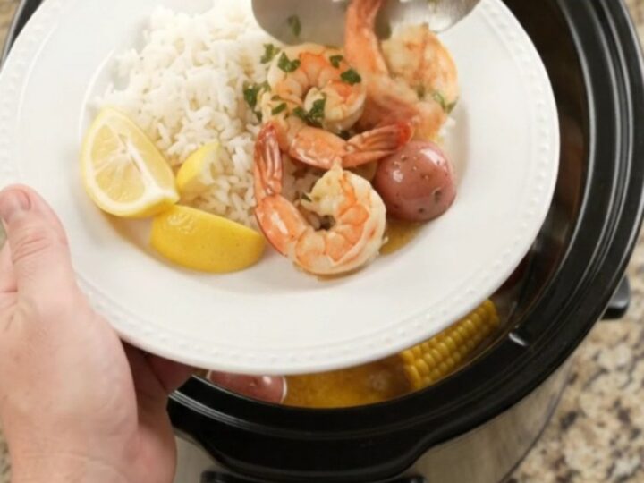 Slow cooker filled with shrimp, corn, and potatoes in a golden butter sauce