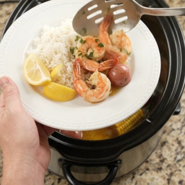 Slow cooker filled with shrimp, corn, and potatoes in a golden butter sauce