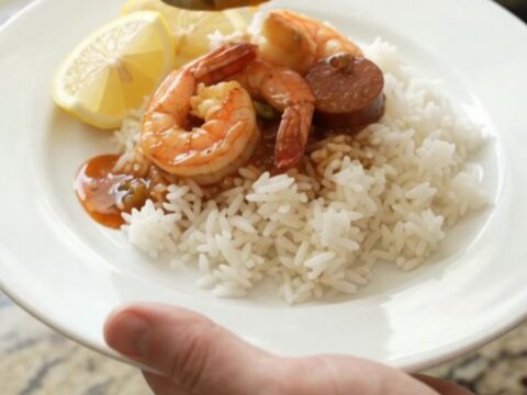 Slow cooker Cajun shrimp and andouille boil in a black crock, with red butter sauce and steam rising.