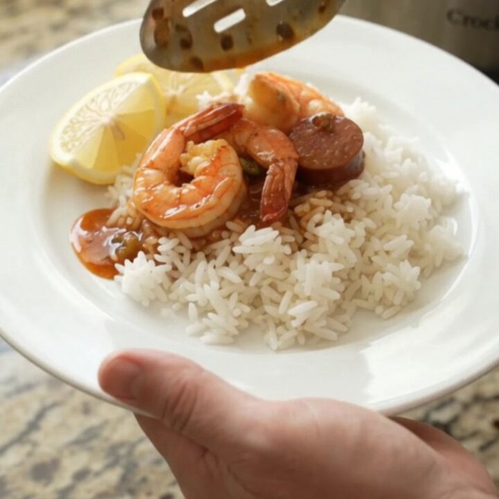 Slow cooker Cajun shrimp and andouille boil in a black crock, with red butter sauce and steam rising.
