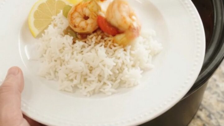A slow cooker filled with jumbo shrimp, bell peppers, and onions in a bubbling red Cajun butter sauce.
