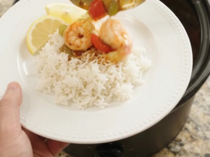 A slow cooker filled with jumbo shrimp, bell peppers, and onions in a bubbling red Cajun butter sauce.