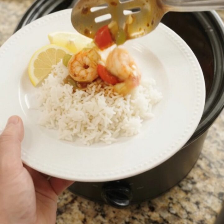 A slow cooker filled with jumbo shrimp, bell peppers, and onions in a bubbling red Cajun butter sauce.