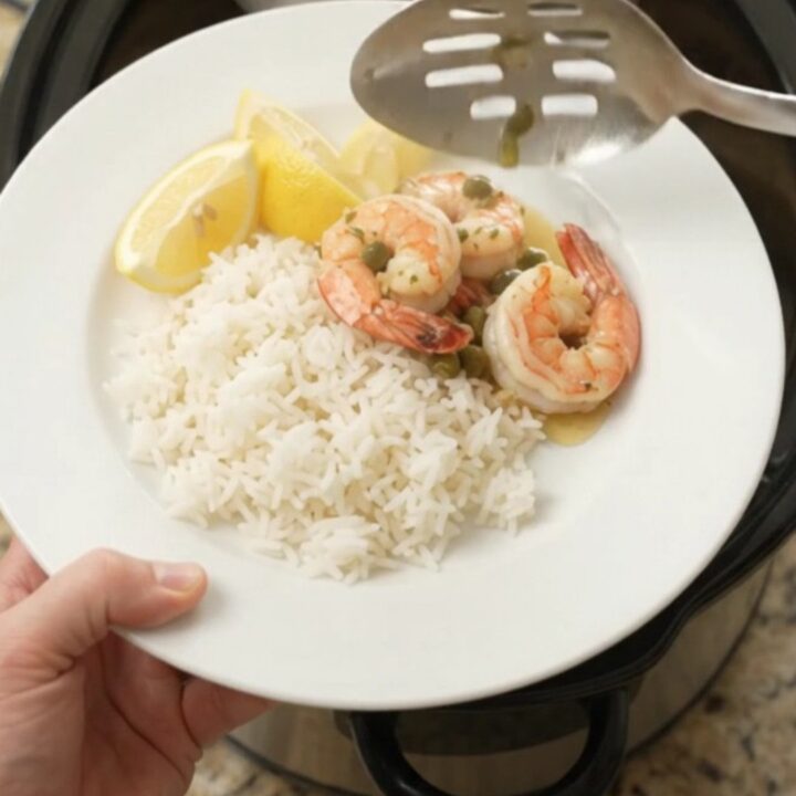 Slow cooker shrimp with lemon, capers, and herb butter in a black crock