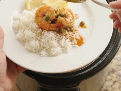 Crockpot full of jumbo shrimp in a bubbling crimson Cajun butter sauce with lemon slices and capers