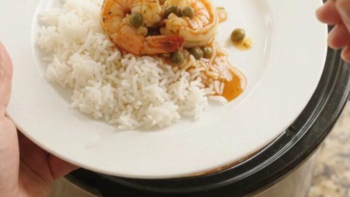 Crockpot full of jumbo shrimp in a bubbling crimson Cajun butter sauce with lemon slices and capers